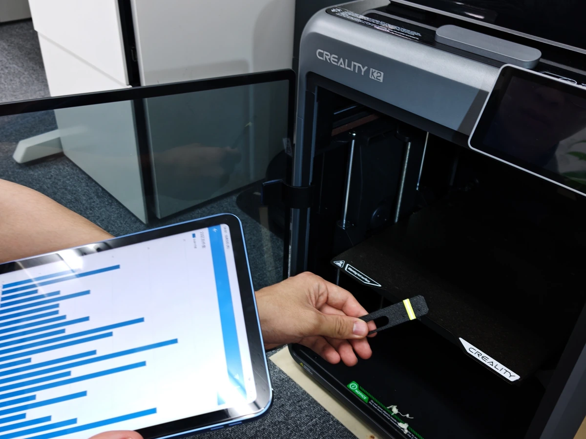 3Dプリンターの前で製作した工具を手に持ち、タブレットを確認する様子