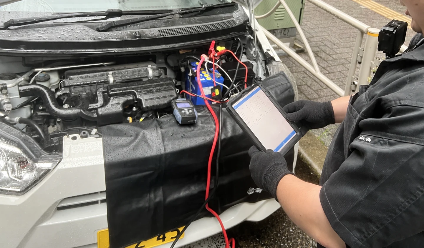 車体を養生し、手袋を着けて測定機器とタブレットを確認する隊員。胸元には記録用カメラ